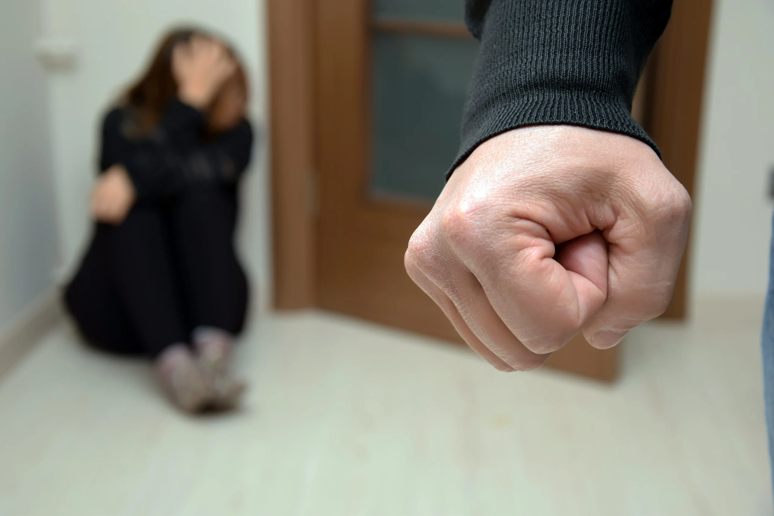 Woman curls in fear before man with fist. If you are facing allegations of domestic abuse, it is important to get in contact with a domestic violence attorney.