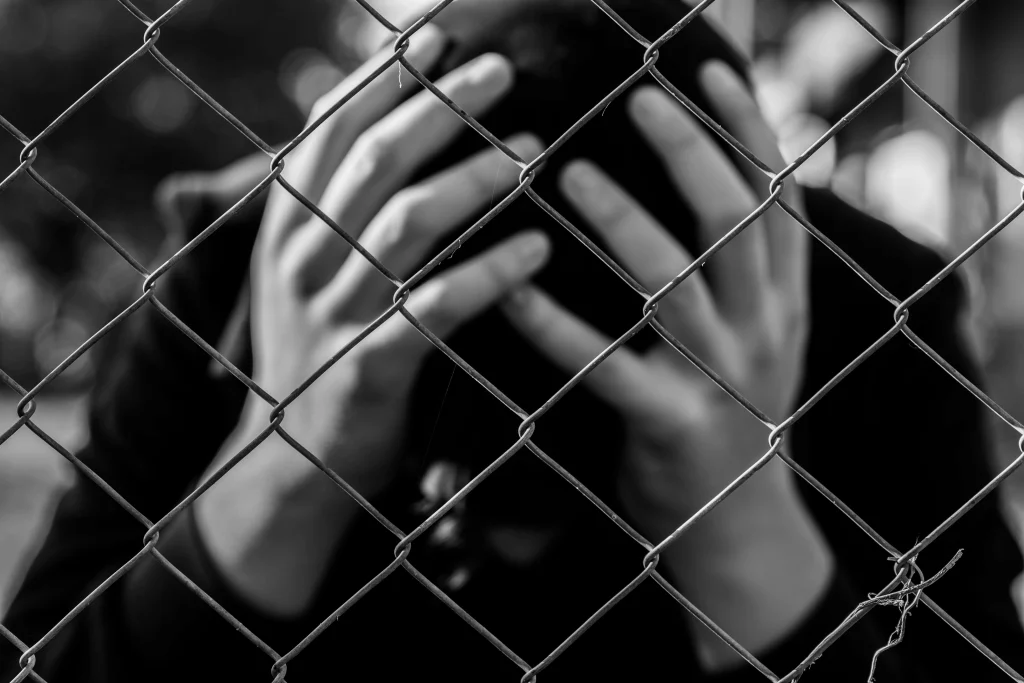 Boy holds head in hands behind a fence. Protect your child’s future and contact us for an experienced juvenile defense attorney in Houston, Texas.