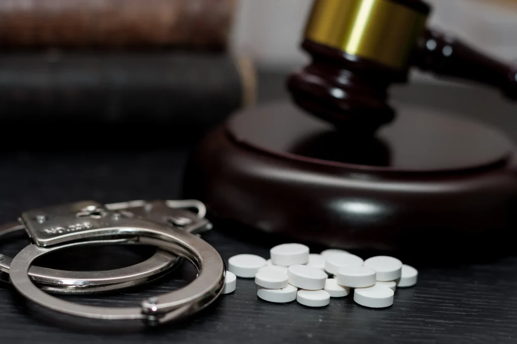 Handcuffs and drug pills sit in front of a justice gavel. Get an experienced drug crimes lawyer in Texas to defend you against serious charges. Call us. 