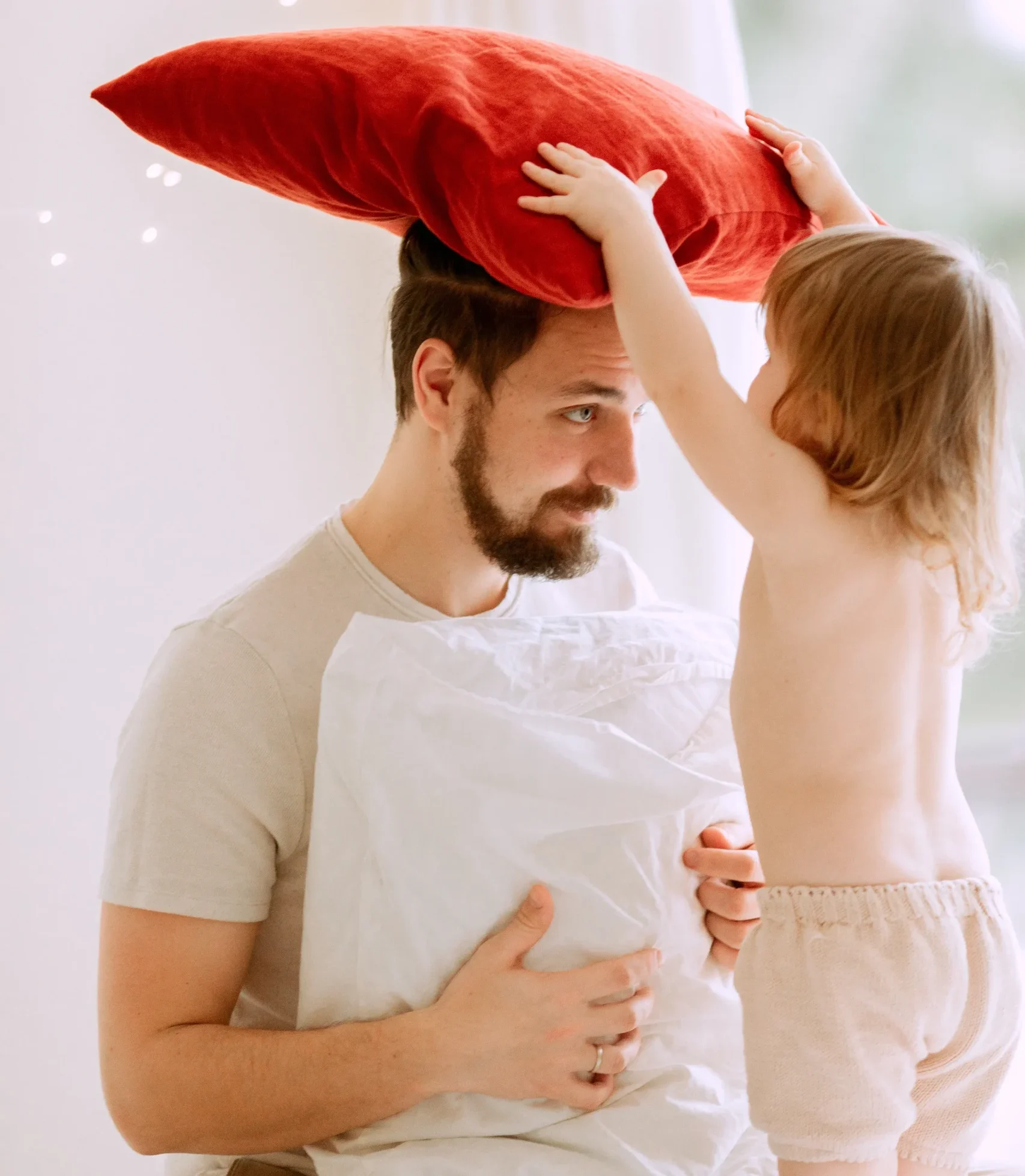 Toddler Daughter placing pillow on her father while they play