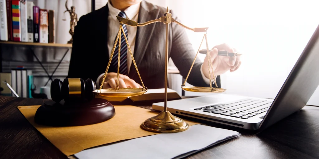 lawyer working at a desk with a laptop, gavel, and justice scales.
